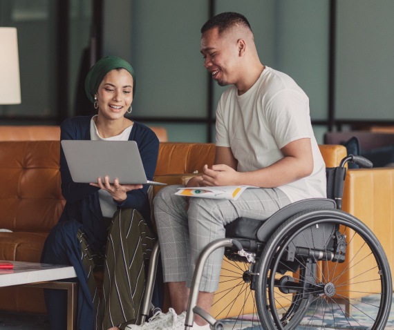 man in wheel chair with women reading laptop