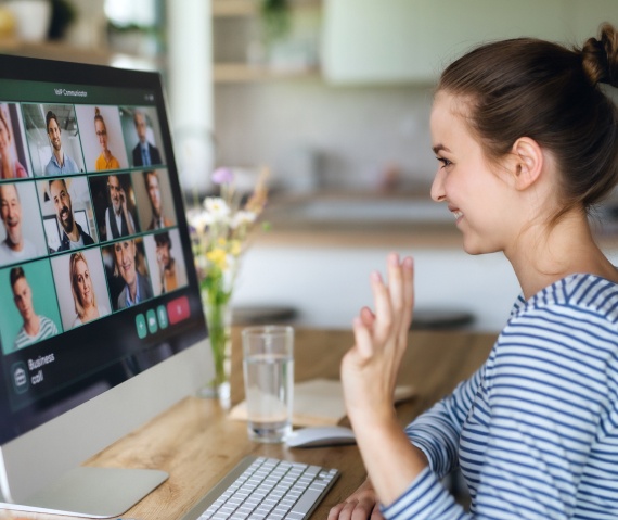 Woman smiling and waving at a group of people in a virtual meeting platform on her computer