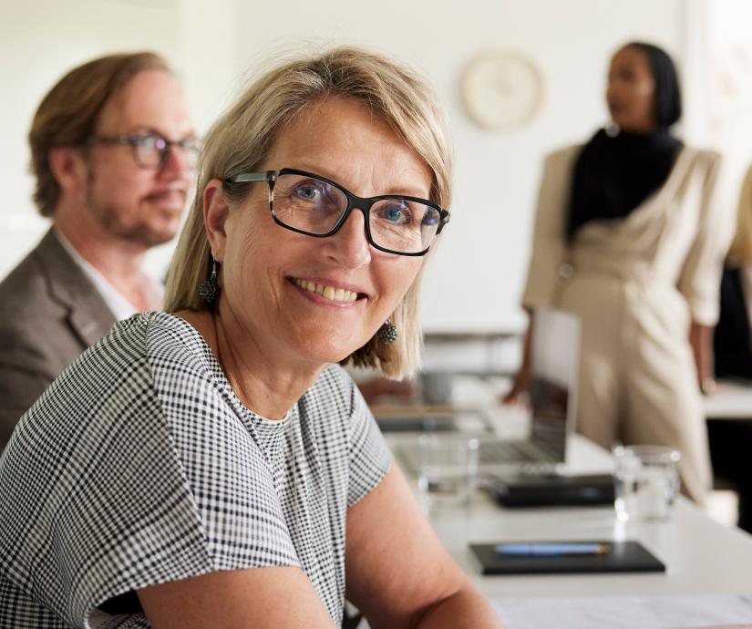 A woman smiling at the camera with a couple people out of focus in the background