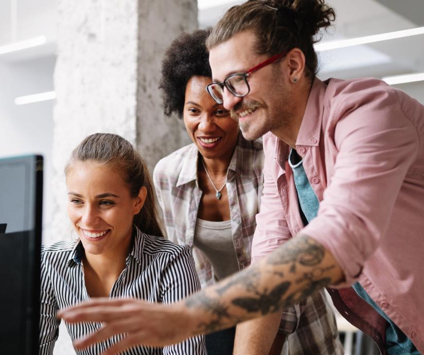 Several people smiling and working together around a computer monitor