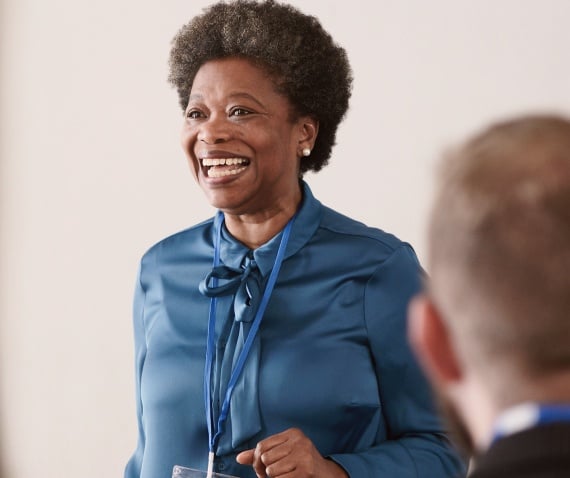 An older woman smiling and presenting to a group off camera