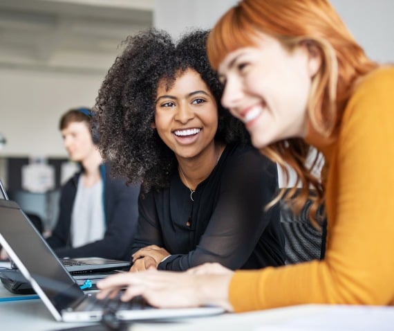 Two women laughing while working on a laptop