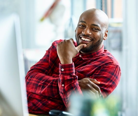 A smiling man leaning back in his chair with his arms crossed