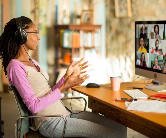 A woman wearing a headset smiling and speaking to a screenful of individuals in a virtual meeting