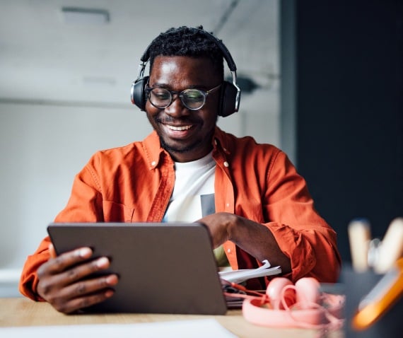 Man wearing headphones and smiling while looking at a tablet